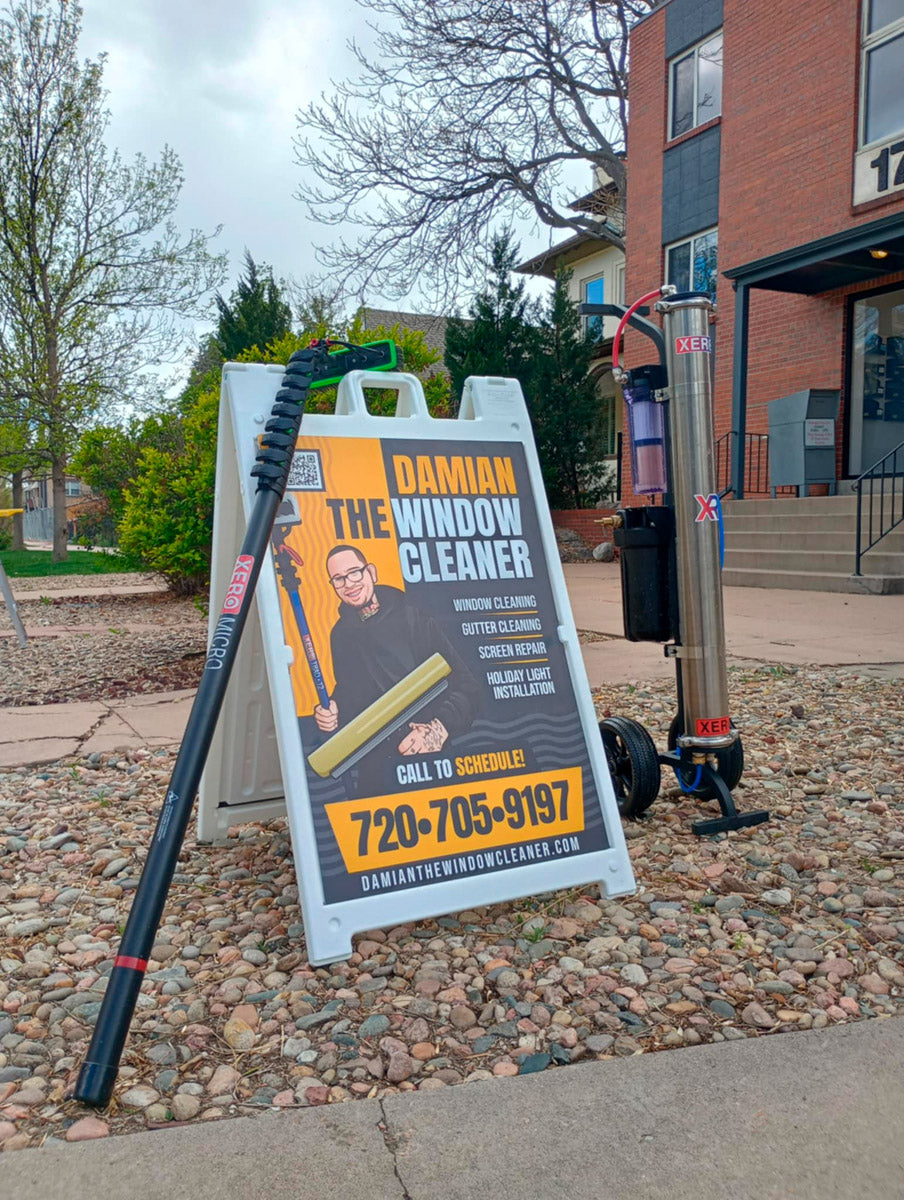 Damian The Window Cleaner A-frame sign displayed outdoors beside XERO water-fed pole and Pure Water System, printed by WCR Marketing.