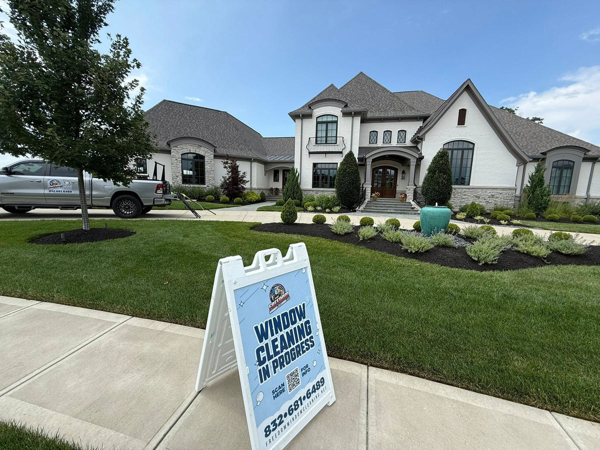 Freedom Window Cleaning A-frame sign positioned in front of a luxury residential home with matching service truck in background, printed by WCR Marketing.