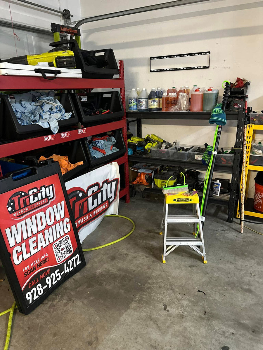 Tri City Window Cleaning red and black A-frame sign shown in workshop surrounded by cleaning tools and WCR supplies, printed by WCR Marketing.