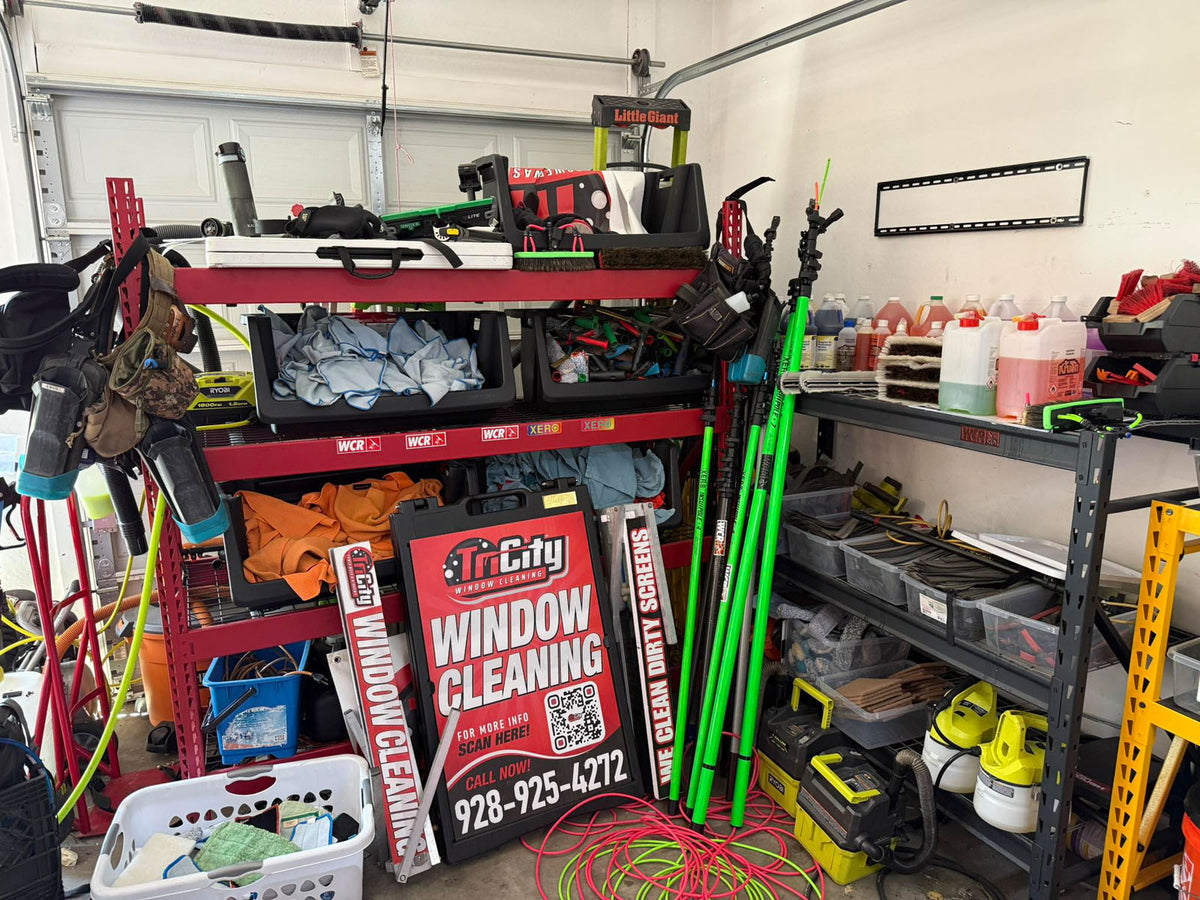 Tri City Window Cleaning A-frame sign photographed in a garage workshop surrounded by tools, poles, and equipment, printed by WCR Marketing.