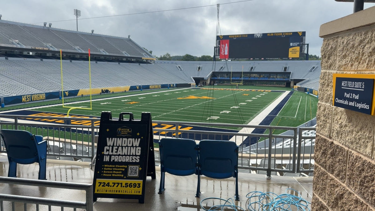 West Window Wash A-frame sign displayed inside large football stadium during commercial window cleaning project, printed by WCR Marketing.