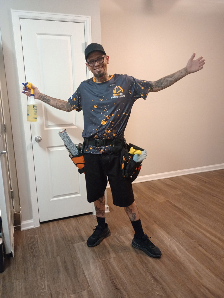 Full-length portrait of technician in branded dye-sublimated jersey, arms outstretched with spray bottle and squeegee belt, printed by WCR Marketing.