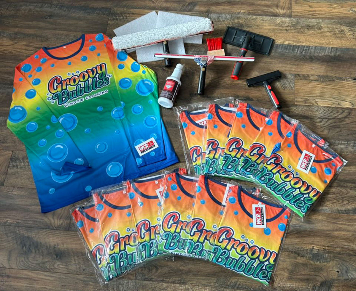 Groovy Bubbles Window Cleaning long sleeve shirts laid out on wooden floor alongside cleaning tools and solution bottles, printed by WCR Marketing.