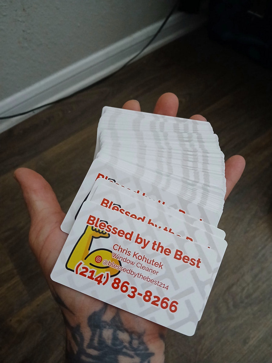 Blessed by the Best business cards held in hand, featuring bold orange font and flexed arm logo for window cleaning services, printed by WCR Marketing.
