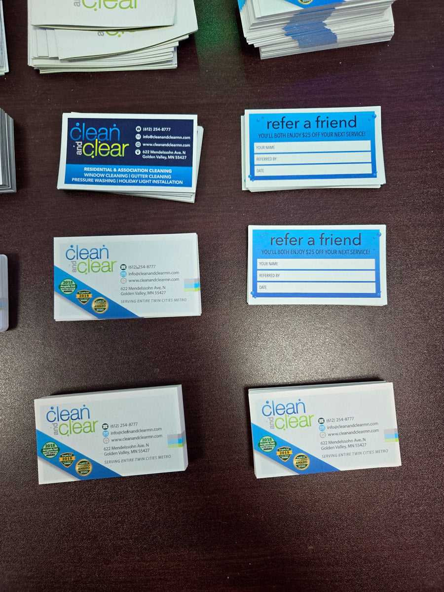 Clean and Clear business and referral cards laid out on dark desk showing blue and green design with service details, printed by WCR Marketing.