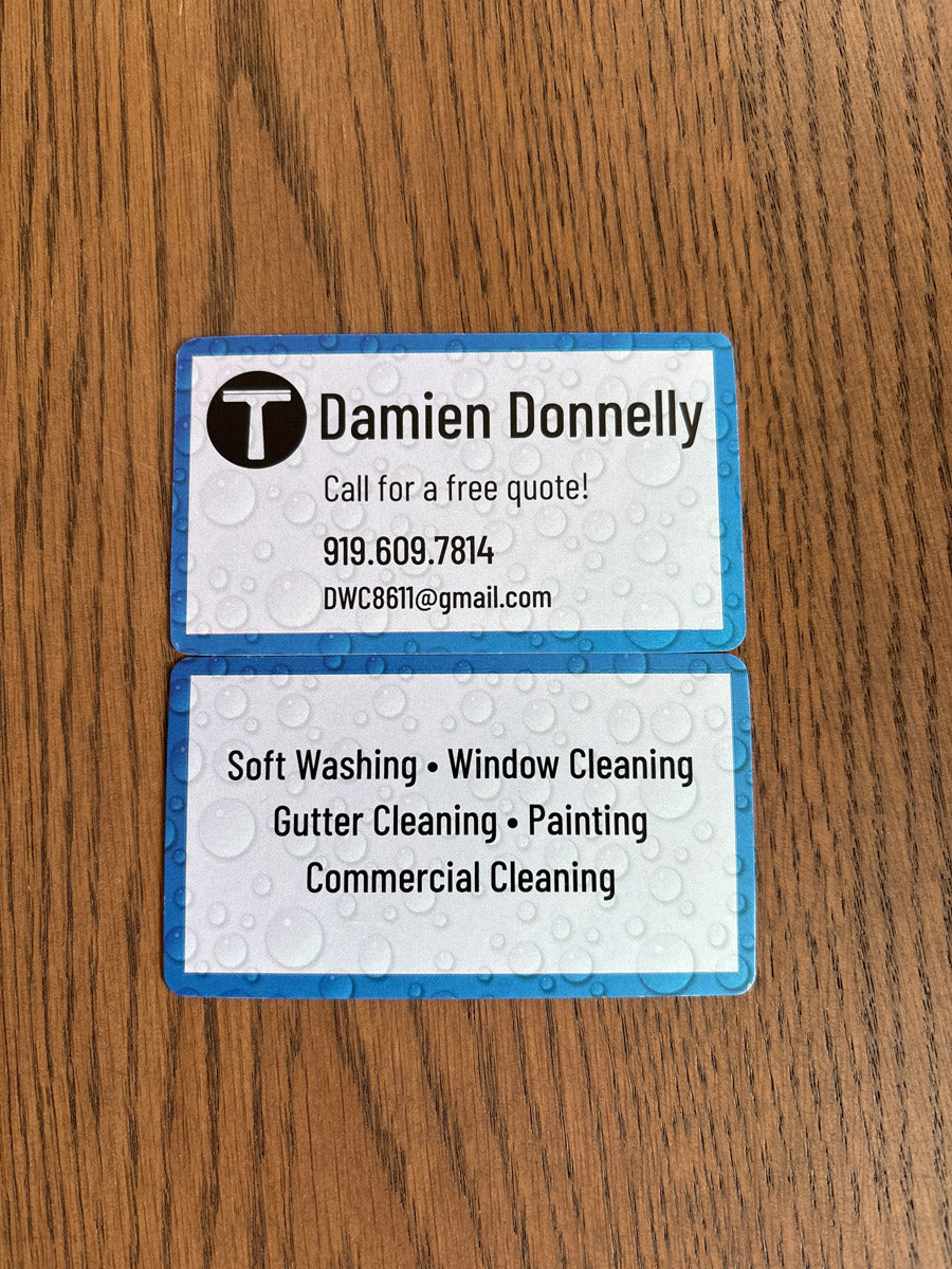 Damien Donnelly business cards displayed on wood surface with blue water-drop background promoting window and gutter cleaning, printed by WCR Marketing.