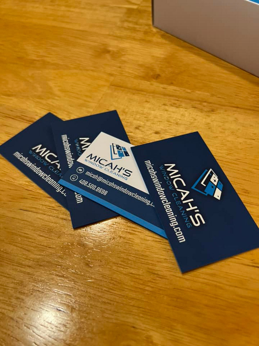 Micah’s Window Cleaning business cards arranged on wooden table showing clean blue and white logo layout, printed by WCR Marketing.