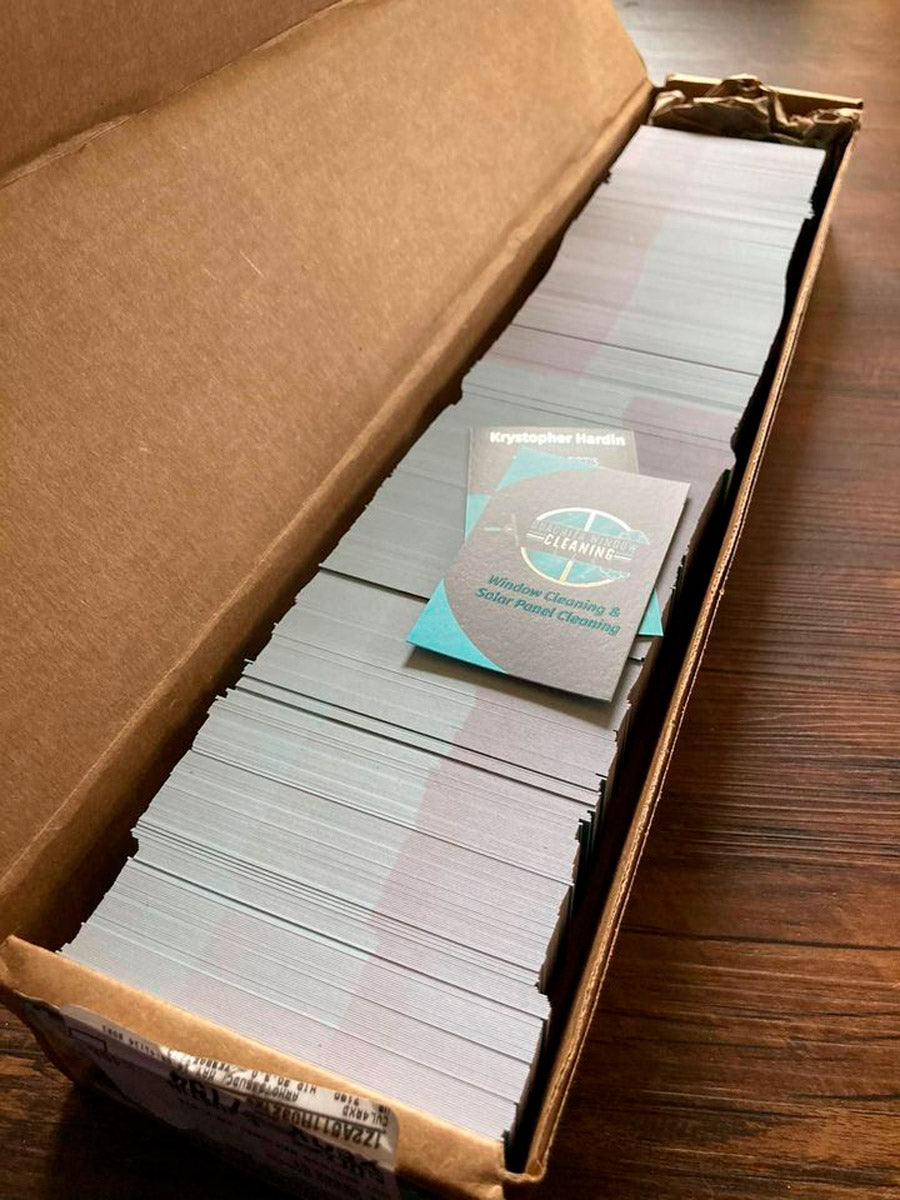 Box of freshly printed Northern Glow Window Cleaning business cards stacked neatly, featuring teal and gray modern design, printed by WCR Marketing.