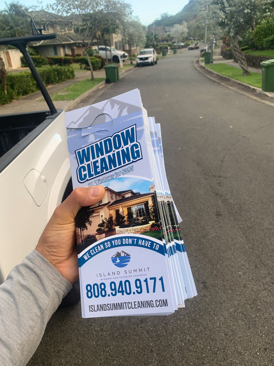 Island Summit Window Cleaning door hangers fanned out and held by hand, advertising window cleaning specials, printed by WCR Marketing.