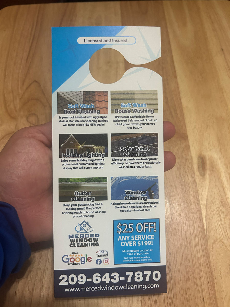 Merced Window Cleaning “Pardon The Glare” door hanger front design displayed on wooden table featuring window image and service list, printed by WCR Marketing.