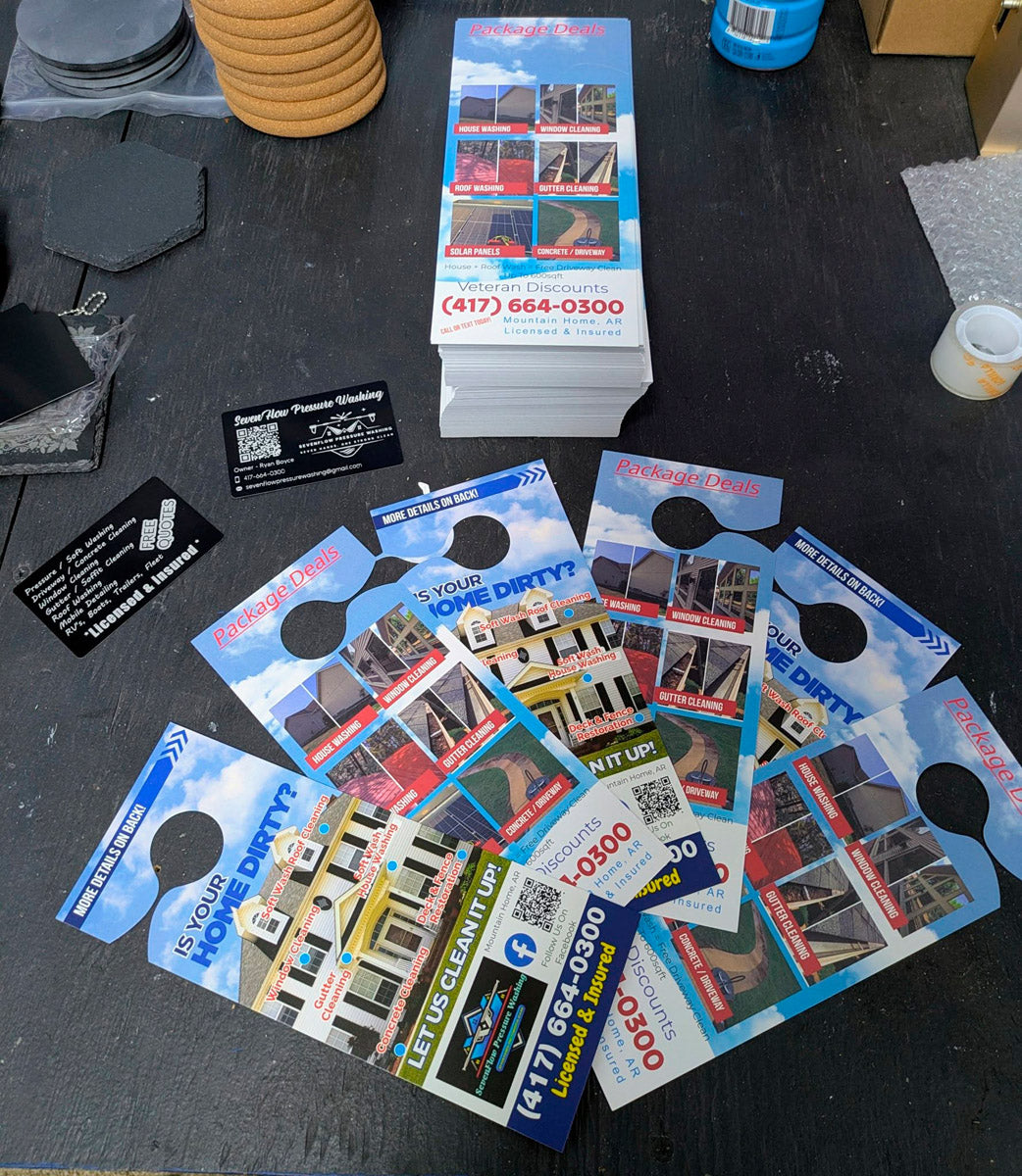 Stack of printed door hangers and business cards for Seven Flow Pressure Washing arranged on workbench, highlighting veteran discounts and service packages, printed by WCR Marketing.