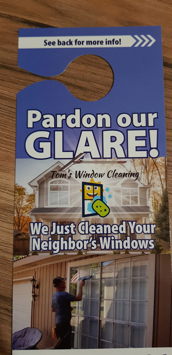 Tom’s Window Cleaning “Pardon Our Glare” door hanger front design showing technician cleaning large home windows, printed by WCR Marketing.