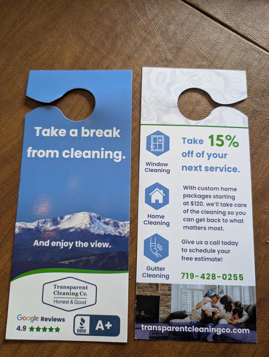Transparent Cleaning Company door hangers displayed on brown leather surface with text “Take a Break from Cleaning” and 15% off offer, printed by WCR Marketing.