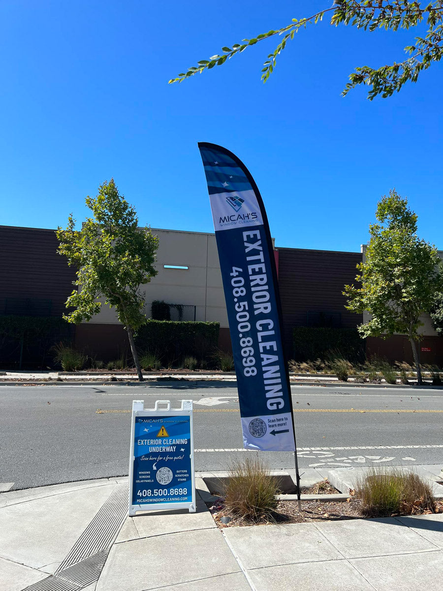 Micah's Window Cleaning feather flag and A-frame sign advertising exterior cleaning set up on a sunny city sidewalk, printed by WCR Marketing.