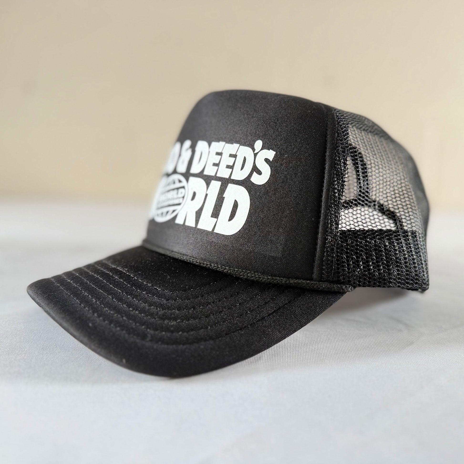 Side angle view of black Goo and Deeds World Enterprises foam trucker mesh hat with mesh back