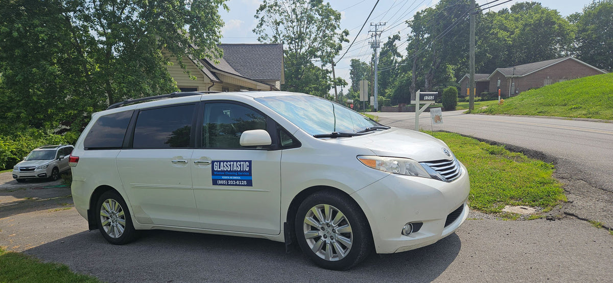 White minivan with a Glasstastic Window Cleaning service magnet parked in a residential driveway, printed by WCR Marketing.