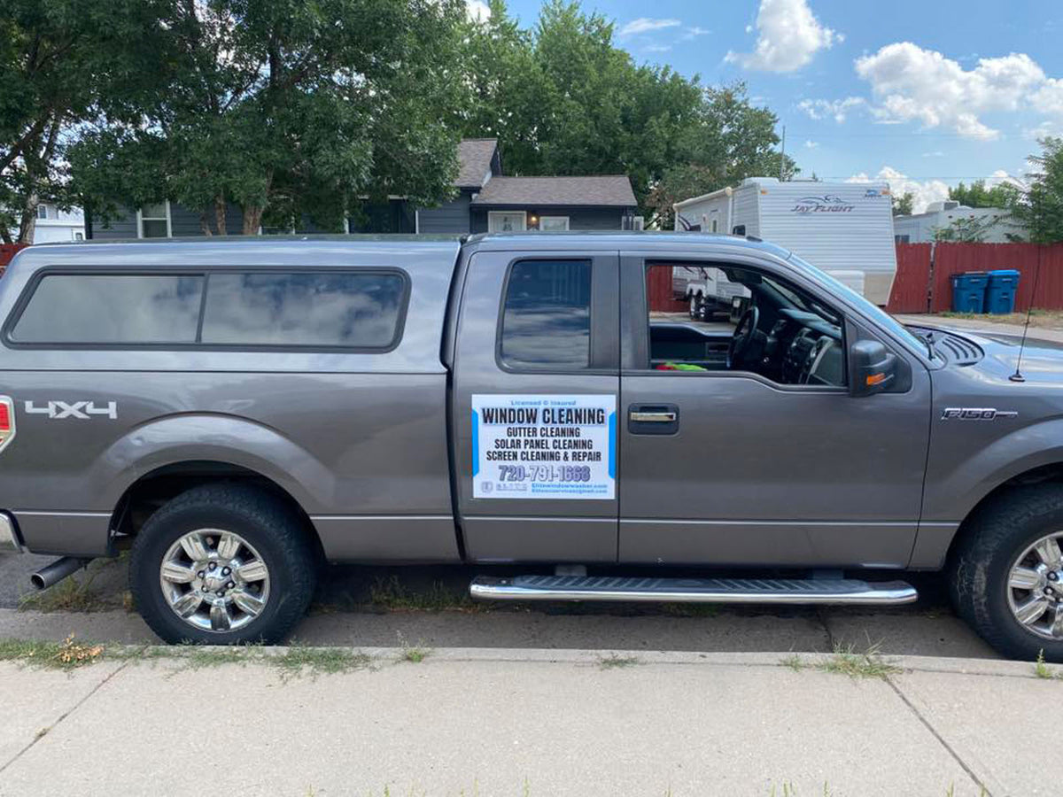 Gray pickup truck parked on a residential street with a window cleaning service door magnet listing multiple exterior cleaning services, printed by WCR Marketing.