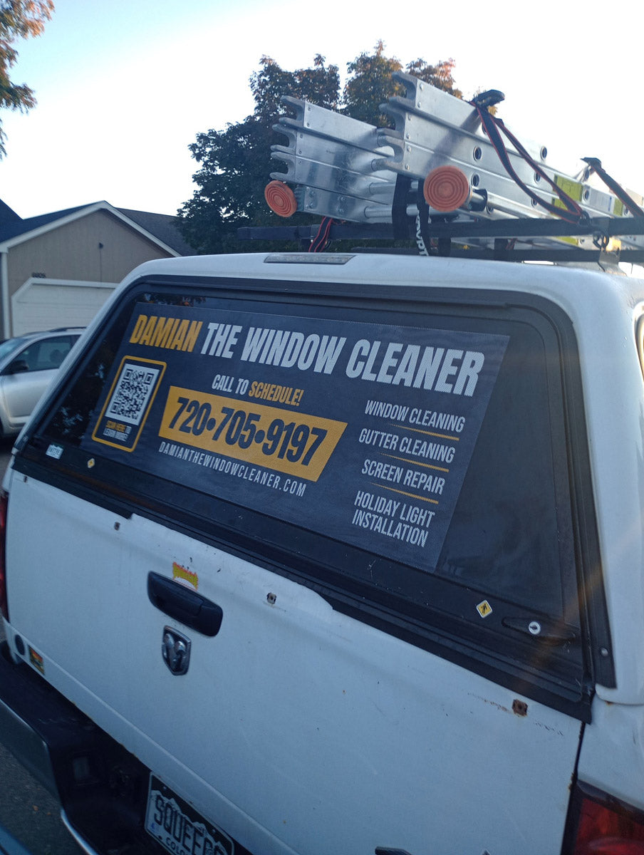 Rear window of Damian The Window Cleaner truck featuring yellow and black vinyl wrap with contact information and service list, printed by WCR Marketing.