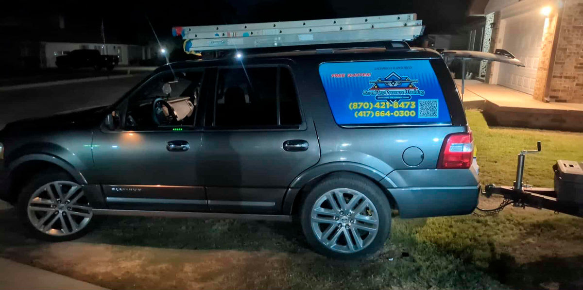 Seven Flag Pressure Washing SUV with roof ladders and vinyl window wrap parked at night near residential driveway, printed by WCR Marketing.