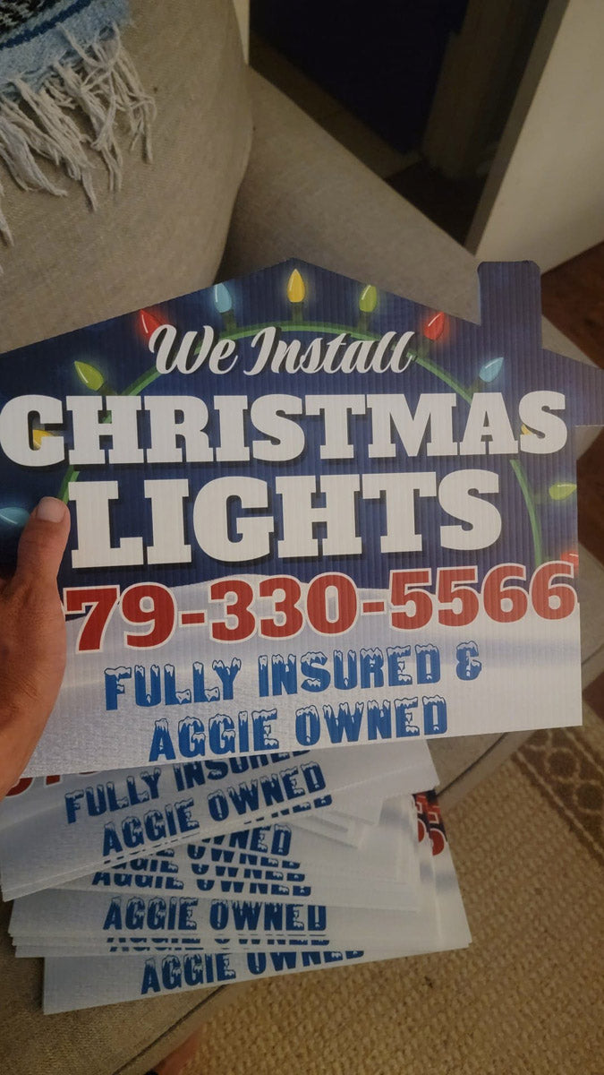 We Install Christmas Lights yard signs with bold lettering and phone number fanned out in a living room, printed by WCR Marketing.