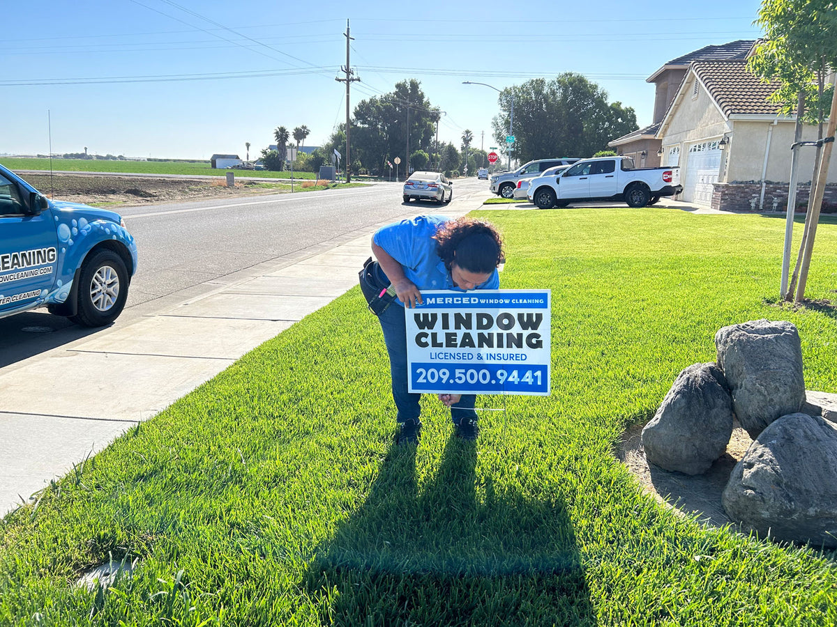 Customer placing a Merced Window Cleaning yard sign on a residential lawn with company vehicle nearby, printed by WCR Marketing.