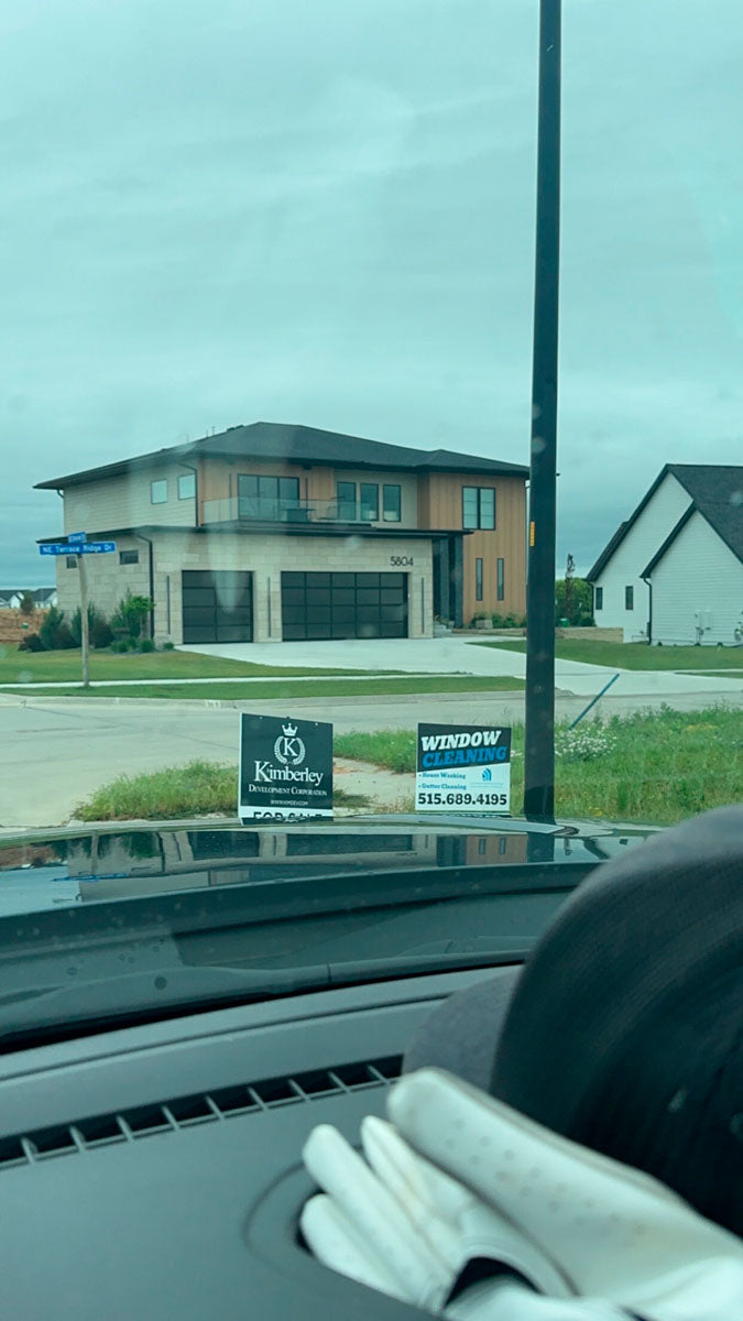 Window cleaning yard sign displayed in front of a new residential development with modern home in background, printed by WCR Marketing.